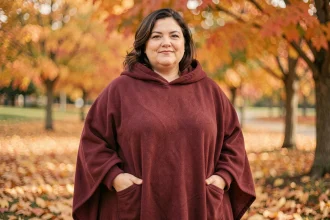 Femme grande taille portant un poncho polaire bordeaux dans un parc automnal aux feuilles dorées