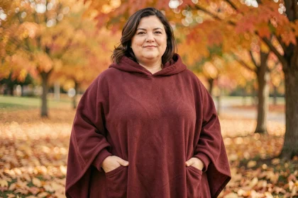 Femme grande taille portant un poncho polaire bordeaux dans un parc automnal aux feuilles dorées